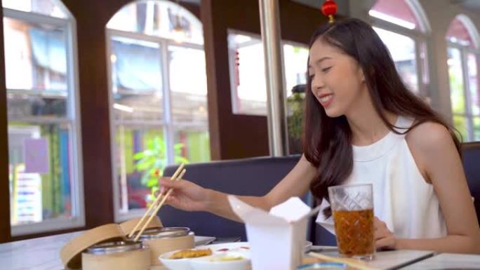 亚洲妇女在独特咖啡馆的餐桌上吃中国菜。旅行女性在餐厅吃饭和享受中餐。餐桌包括咸味食物和传统中式甜点。