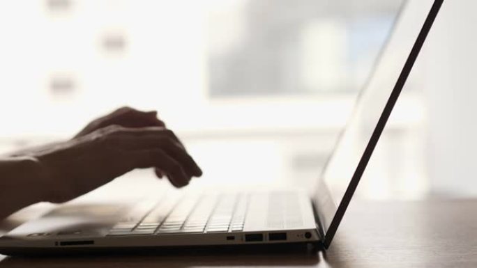 女性博客自由职业者在家庭办公室工作笔记本电脑。用键盘关闭女性的手。女人在窗户旁边的台式机上使用笔记本