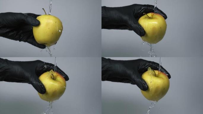 用水花在灰色背景上洗净手中的青苹果，慢动作。男人戴着黑色手套握住青苹果，在水流下洗净
