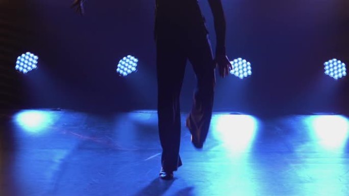 跳舞伦巴元素的男舞者的剪影。舞厅舞者正在一个充满烟雾和灯光的黑暗工作室里，在镶木地板上练习拉丁美洲舞