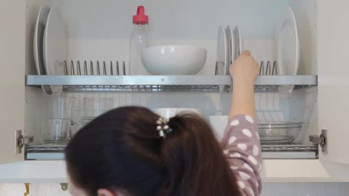 女人清洗盘子，把它们放在厨房橱柜里，白色的盘子和杯子在厨房里晾干。