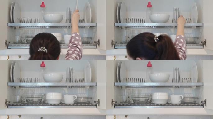 女人清洗盘子，把它们放在厨房橱柜里，白色的盘子和杯子在厨房里晾干。