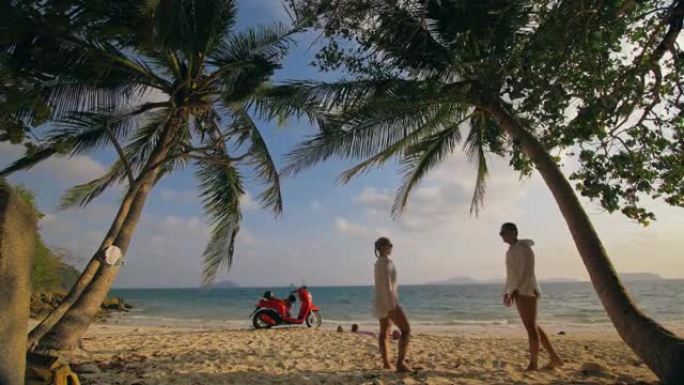 滑板车公路旅行。沙滩上穿着白色衣服的红色摩托车上可爱的夫妇。人们走在热带棕榈树、大海附近。摩托车租金
