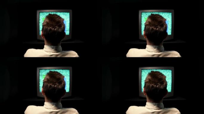 一个男人坐在黑色背景的黑暗演播室里的旧电视前的后视图。噪音干扰或电视监视器上的线路，破损和废弃的复古