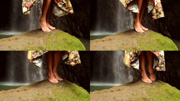 站在瀑布附近的石头上的优雅女孩的腿特写