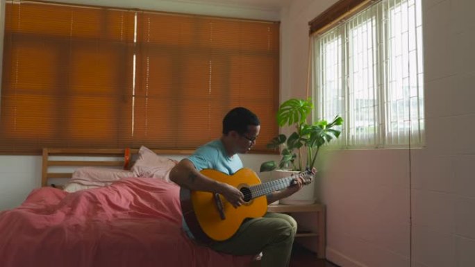电影拍摄的独立亚洲男子在卧室弹吉他，房间里有植物。感觉不错。