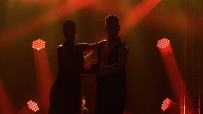 在黑暗的工作室里，烟雾和明亮的红色霓虹灯之间优雅的阿根廷探戈。由热情的舞伴表演的舞蹈表演。轮廓。特写