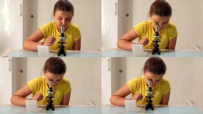 一个穿着黄色t恤的可爱少女正在透过显微镜看