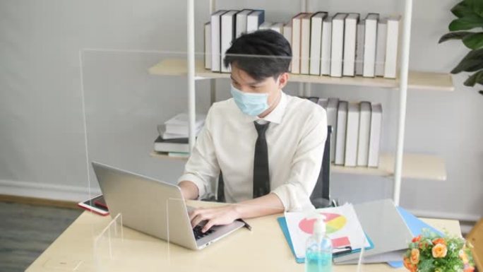 办公室工作的新常态，年轻商人使用防护面罩和丙烯酸隔墙
