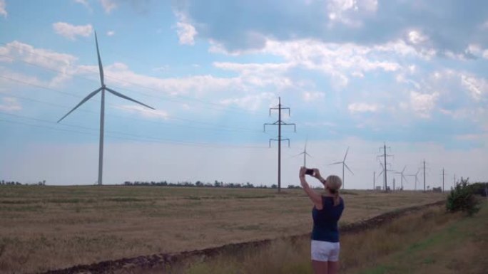 一个女孩在智能手机上拍摄风力发电机