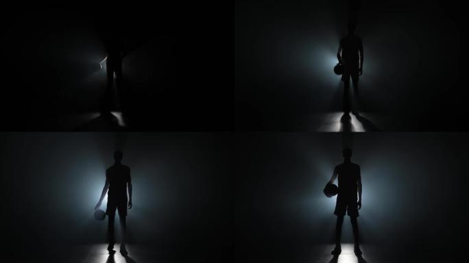 在黑暗和烟雾中，盖伊的身影直接走进相机，手里拿着一个篮子球。篮球运动员在工作室里用背光摆姿势。慢动作