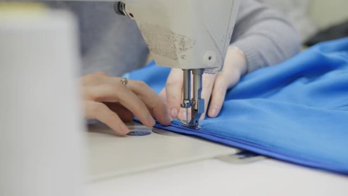 缝纫车间。女人在工业缝纫机上缝纫。双手特写。将拉链插入产品中。