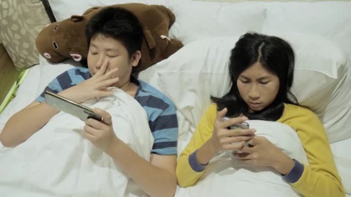 快乐的亚洲儿童在假期期间在酒店房间的床上一起玩网络游戏，生活方式理念。