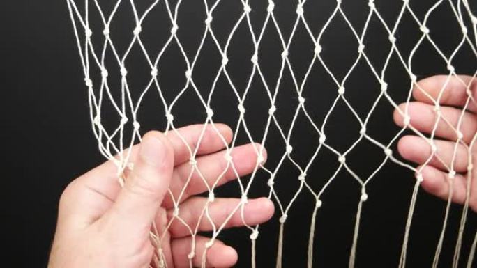 人员从黑色背景的白色合成绳中检查手动编织网的质量。