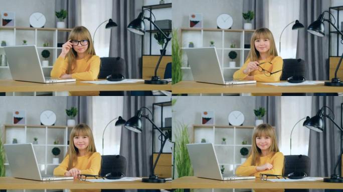 好看快乐快乐时尚的10岁女孩，金色长发，坐在电脑前学习课程时在相机上摆姿势