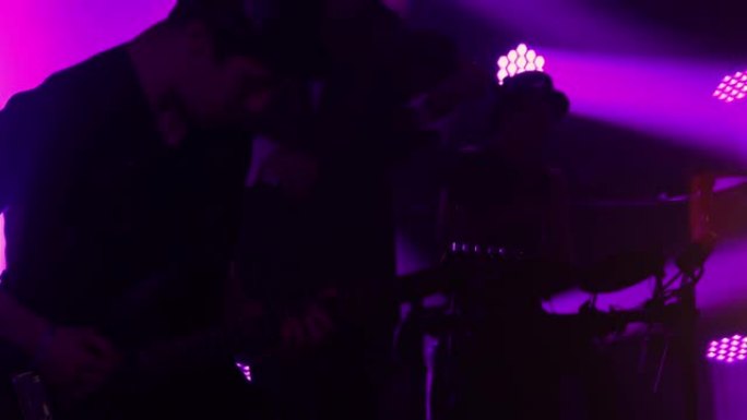 摇滚乐队充满活力的现场音乐会。一队音乐家在烟雾和动态的紫色灯光中，在黑暗中动态演奏小提琴，电吉他和鼓