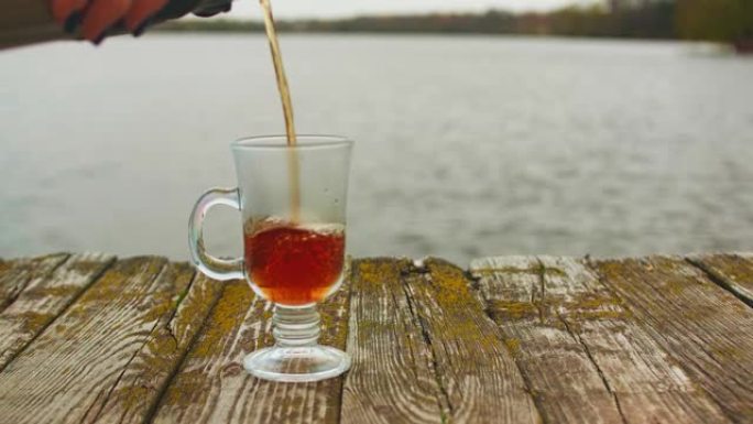 旧木皮上的爱尔兰咖啡杯视图。茶被倒入其中。背景下的河流和森林散焦视图。
