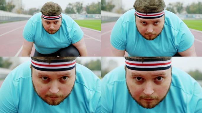 迷人的年轻人肥胖，在起跑线的体育场外准备开始努力奔跑。在阿里·阿列克谢迷你上拍摄