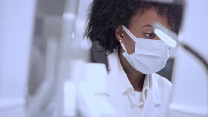非洲民族，在实验室使用显微镜的女性医生。用防护面罩关闭脸部。浏览实验室玻璃器皿