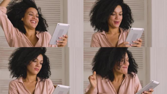 可爱的非洲裔美国妇女在数字平板电脑上寻找信息，并快乐地庆祝胜利，收到了好消息。黑人女性坐在灯光室。特