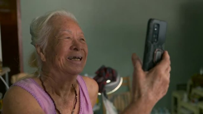 快乐的亚洲高级女性在家中使用智能手机vdo呼叫检疫的电影拍摄。