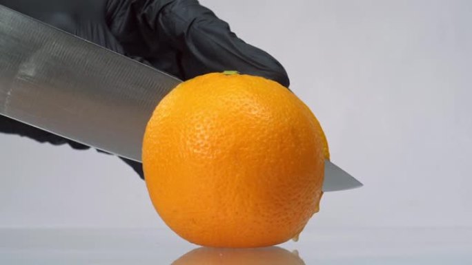 戴着黑手套的男人用白色背景上的大刀将橙色水果切成薄片。慢动作切割