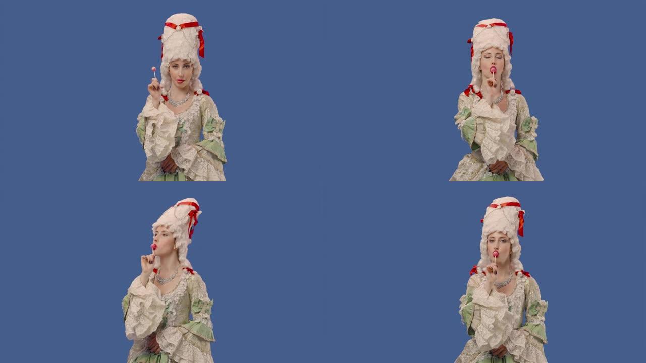穿着白色复古蕾丝连衣裙和假发的朝臣女士肖像，享受甜美的糖果棒棒糖。年轻女子在工作室摆姿势，蓝屏背景。