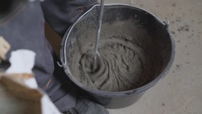 人正在桶里搅拌灰色混凝土和底漆。桶中的混合灰色混凝土和底漆-翻新。腻子溶液混合在黑色桶中。