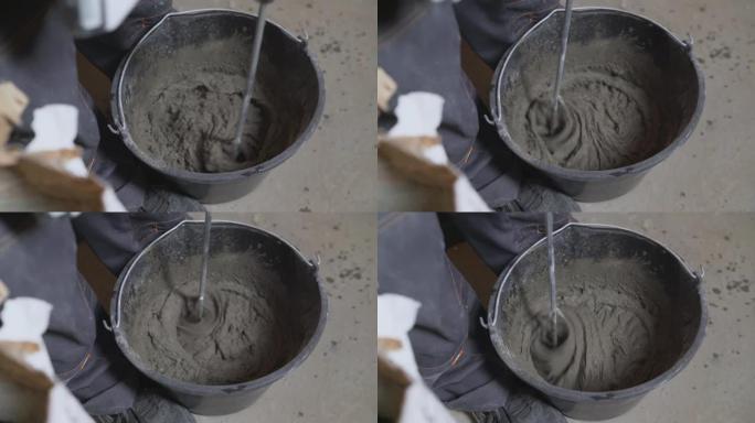 人正在桶里搅拌灰色混凝土和底漆。桶中的混合灰色混凝土和底漆-翻新。腻子溶液混合在黑色桶中。