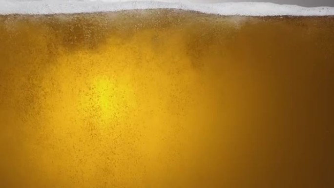 一杯啤酒内容物的特写。啤酒慢慢倒入玻璃杯中，引起大量气泡，波浪和泡沫。