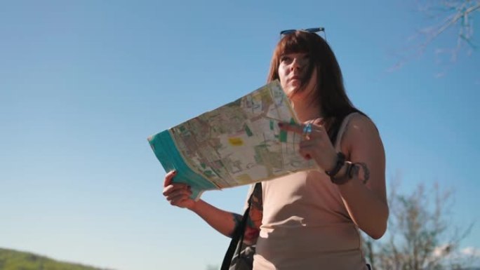 一个白人妇女的肖像站在路边，看着一张纸质地图。底视图。本地旅行和搭便车的概念