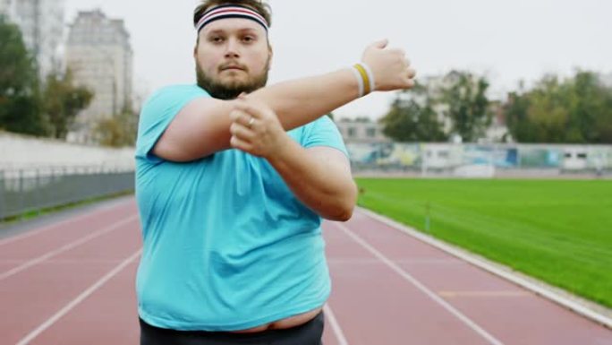 健康的生活方式概念肥胖的人在开始在体育场跑步之前伸展双手，他非常兴奋。在阿里·阿列克谢迷你上拍摄