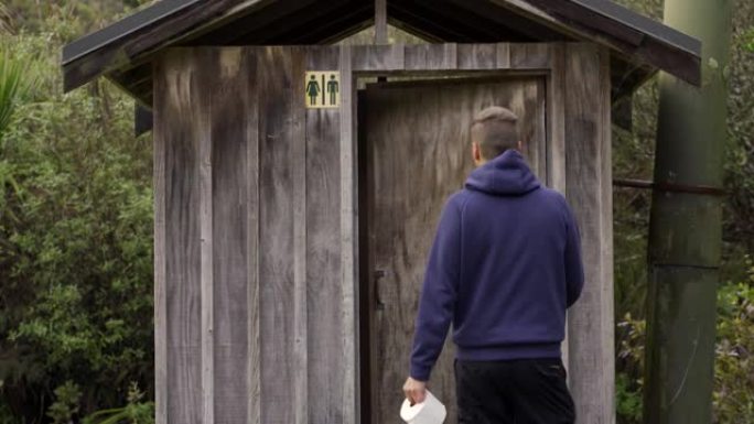 男子在室外公共厕所开门进入森林并拿着纸厕所