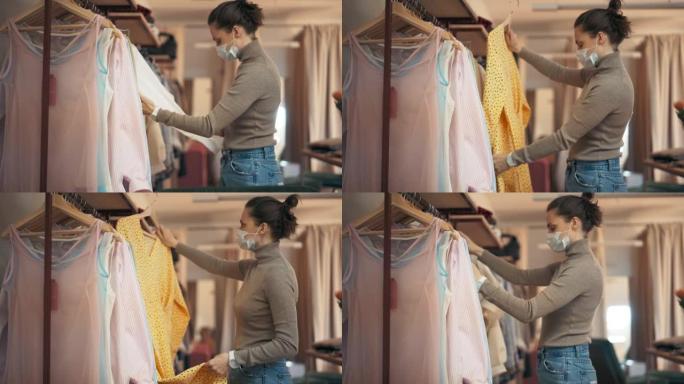 一名戴着口罩的年轻女子在商店检查衣架上的衣服