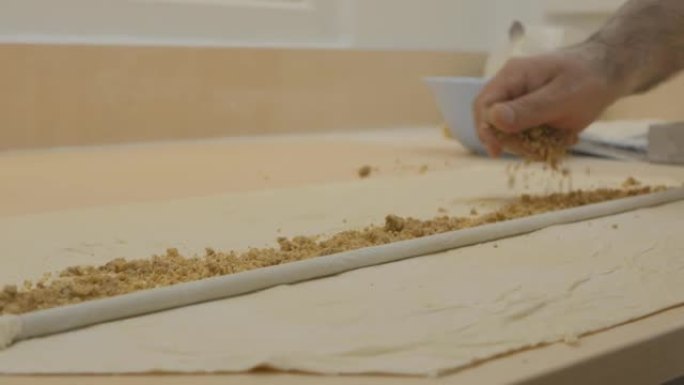 东方面包师将磨碎的坚果馅料倒在面团上，然后向内滚动。他准备果仁蜜饼