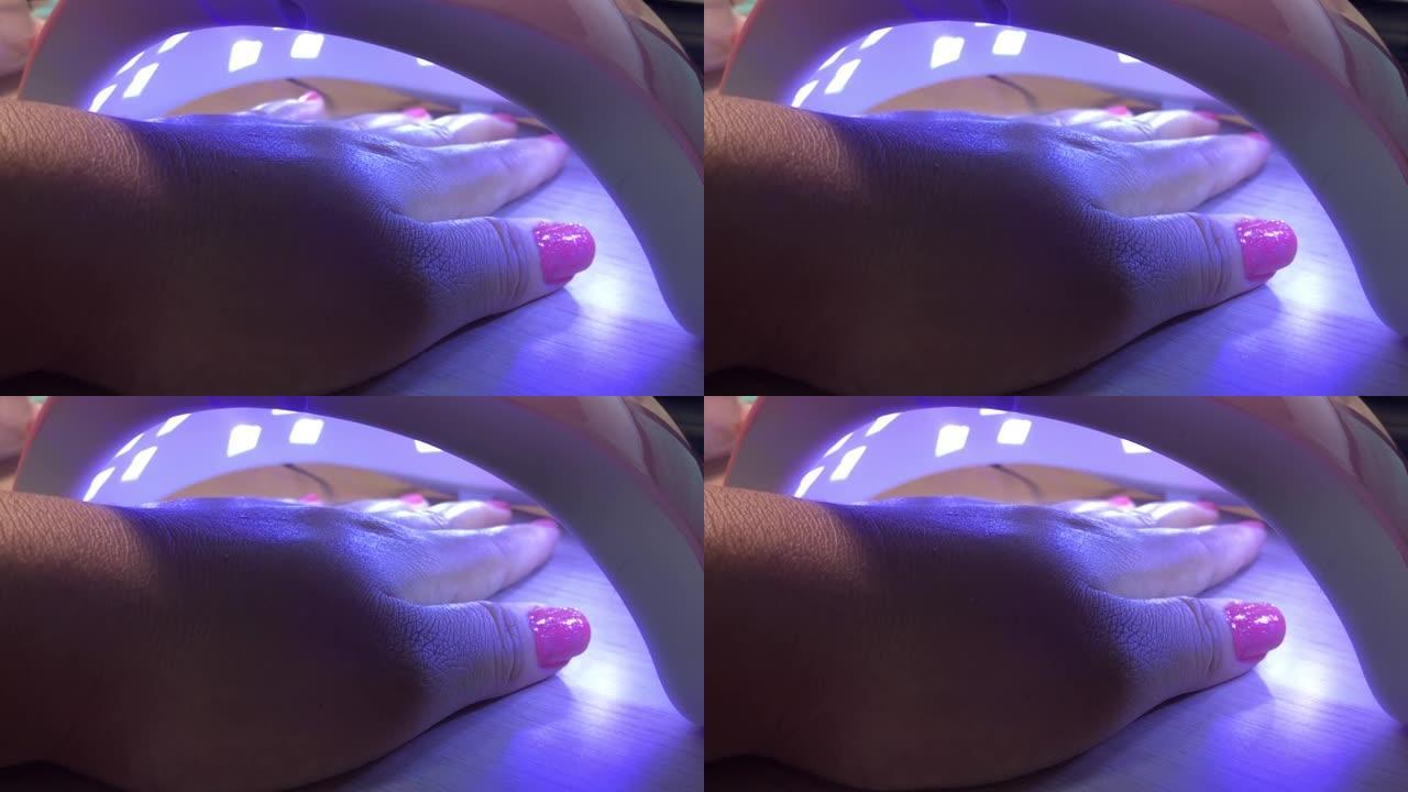 灯下的女人指甲。在紫外线灯中指甲疼痛的女人的手。自制美甲服务化妆理念。带有噪音和burry boke