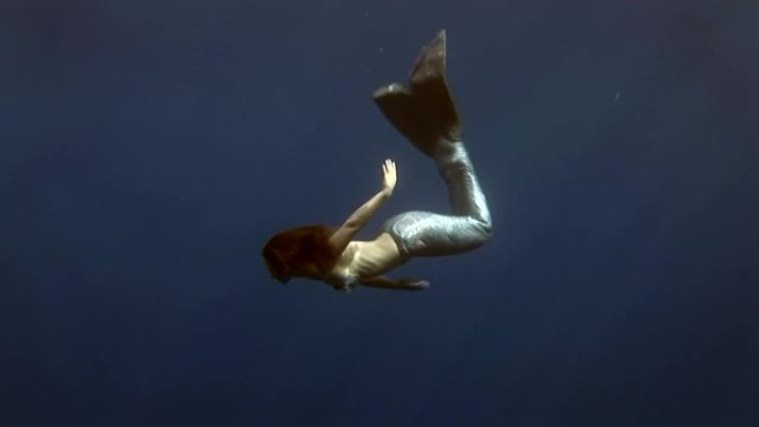 蓝色背景的年轻女孩模特水下美人鱼服装在红海摆姿势。