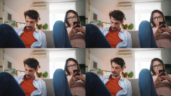 一对白人夫妇坐在家里的沙发上玩着智能手机
