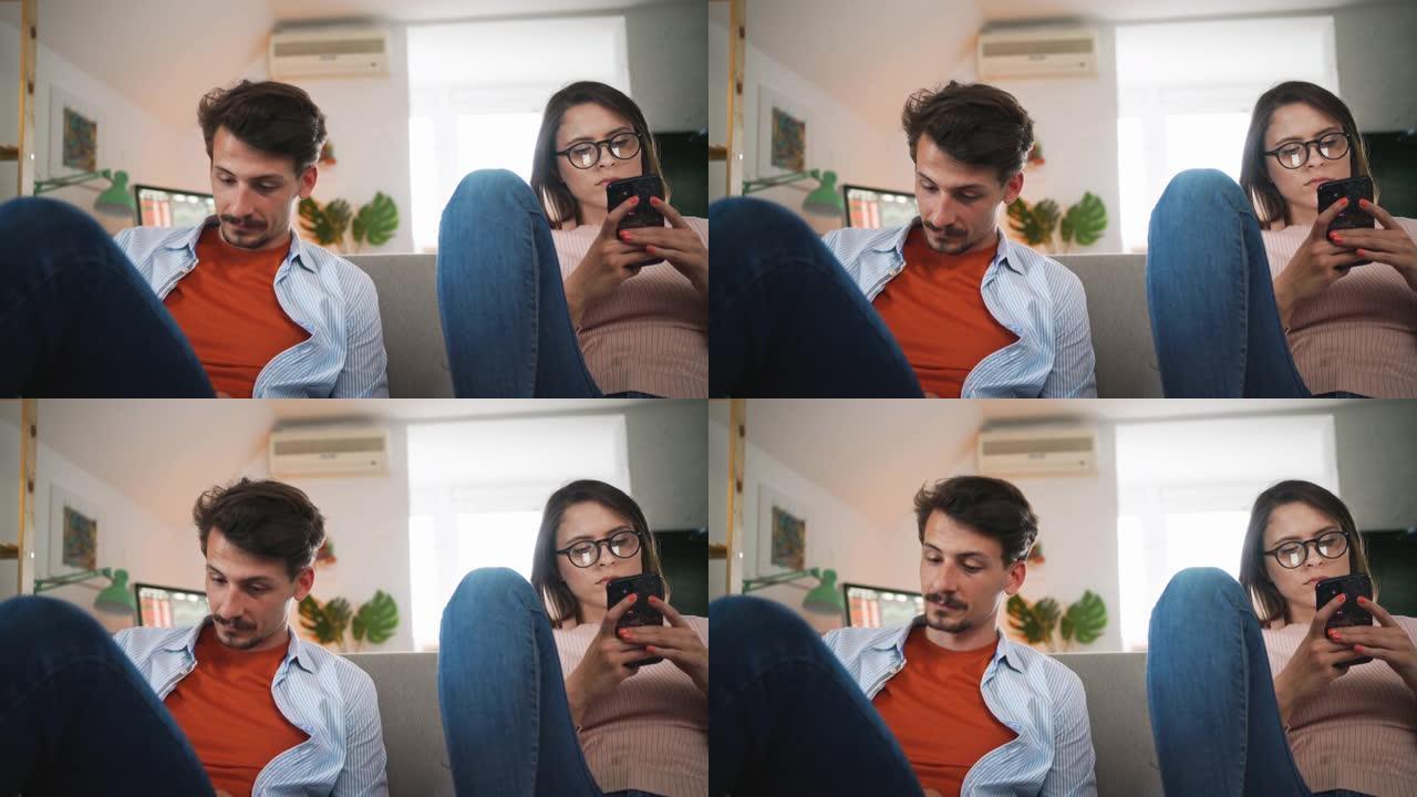 一对白人夫妇坐在家里的沙发上玩着智能手机