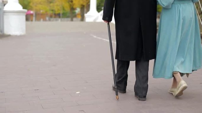 穿着黑色外套的成熟男人和他的妻子沿着公园小巷散步。