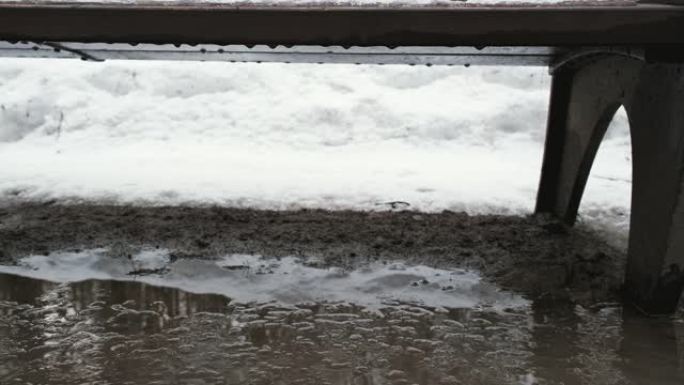 公园长凳特写镜头。雪融化，水滴从长凳上掉入水坑