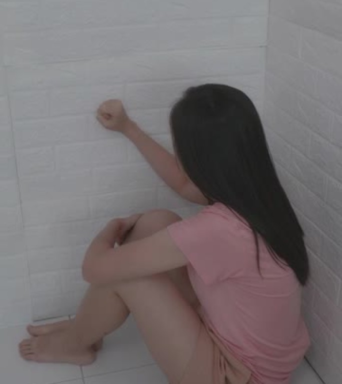 一个20-30岁的女人穿着休闲装坐在房间的一个小角落里，为被男友分手而哭泣。