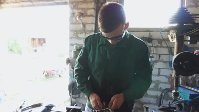 在车间使用工具修理汽车细节的防护眼镜的男机械师。穿着制服的专业修理工在他的车库里工作。维护服务的概念