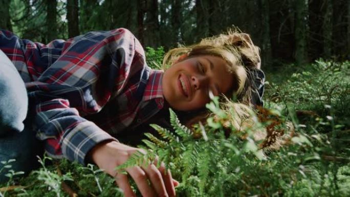 游客在夏季森林的草地上放松。年轻女子躺在树林中的地上