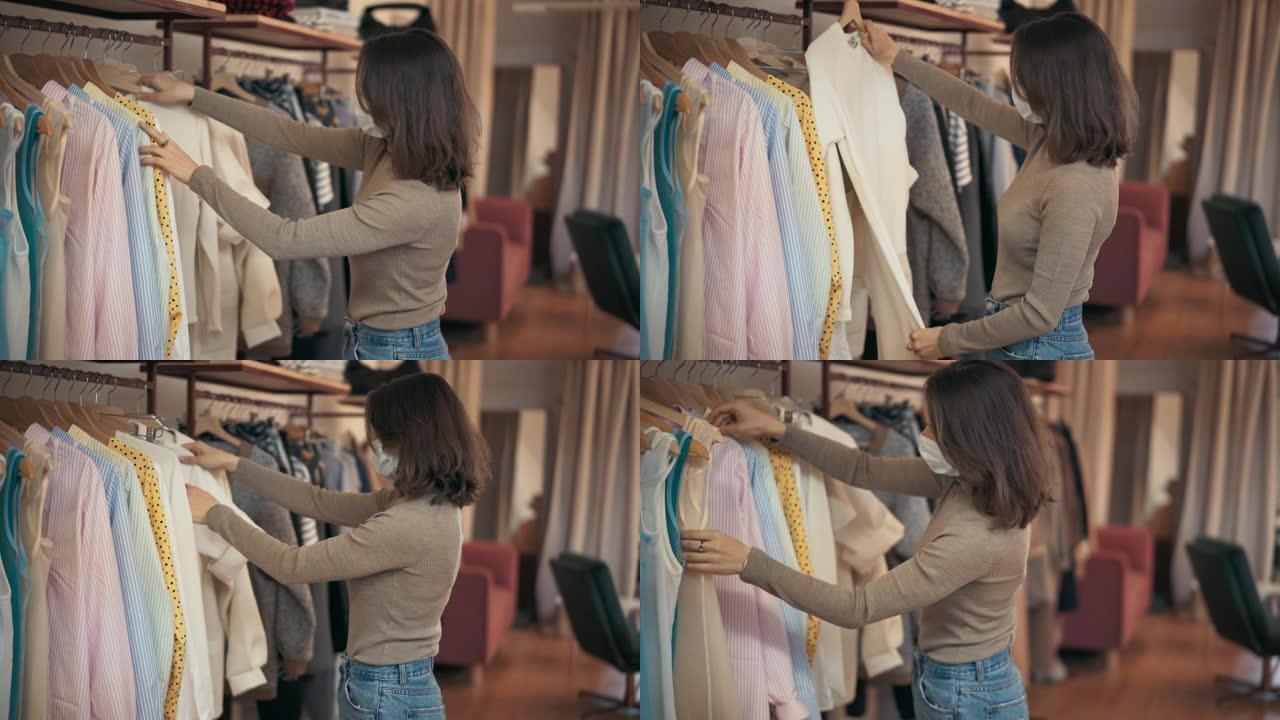 一名戴着口罩的年轻女子在商店检查衣架上的衣服