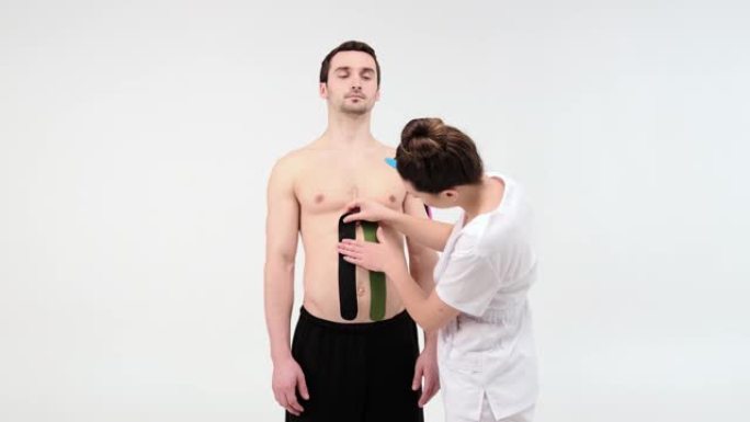 女性治疗师在浅色背景上在男人的腹部上应用运动学胶带。女人准备男性患者将kinesio胶带粘在他的腹部