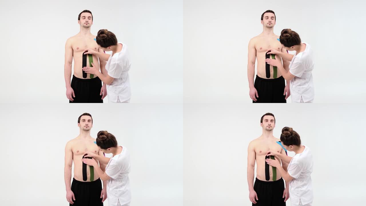 女性治疗师在浅色背景上在男人的腹部上应用运动学胶带。女人准备男性患者将kinesio胶带粘在他的腹部