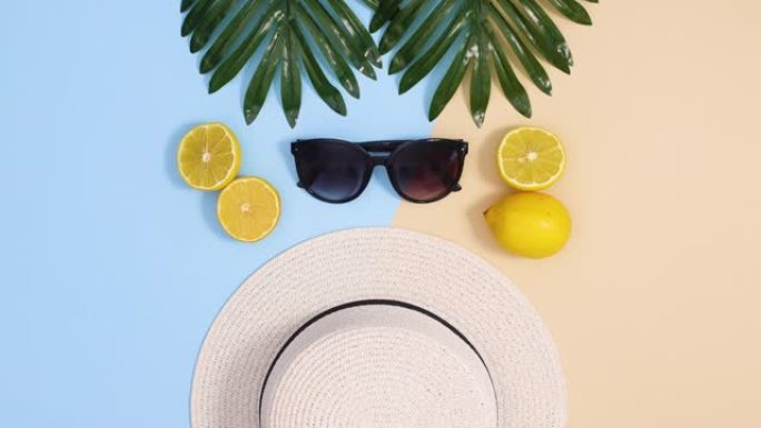 夏季热带停止运动平躺。异国情调的叶子，帽子，太阳镜和柠檬出现在蓝色的沙质背景上