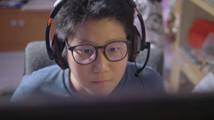 快乐的亚洲青春期男孩在家用带发光二极管灯的电脑玩网络游戏，生活方式概念。