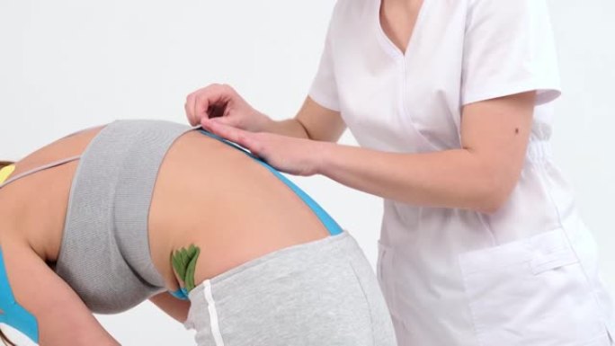 理疗师将kinesio胶带贴在女性患者的小背部，运动学胶带，运动学疗法，运动员受伤后正在康复。